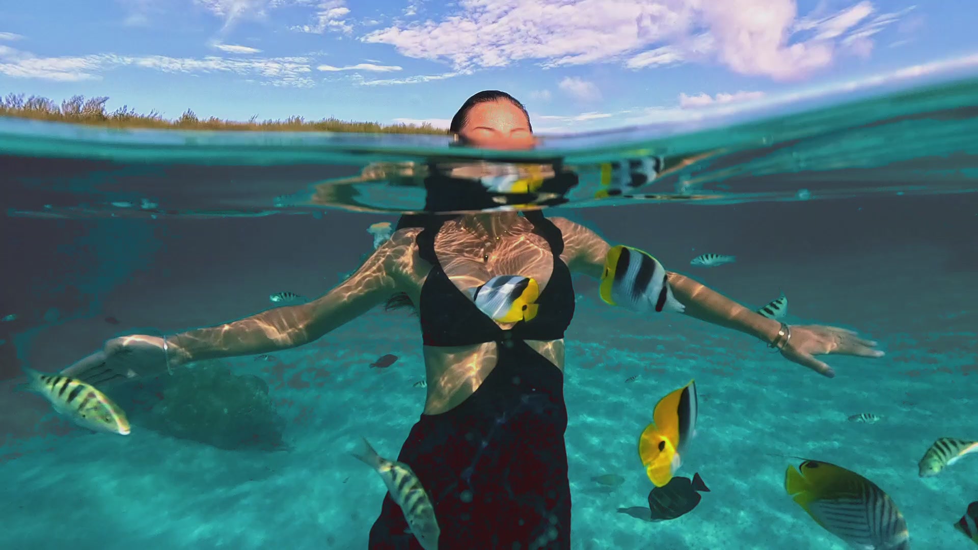 Load video: A woman on a beach wearing a convertible dress that changes into a swimsuit. The video shows both versions in a tropical setting.